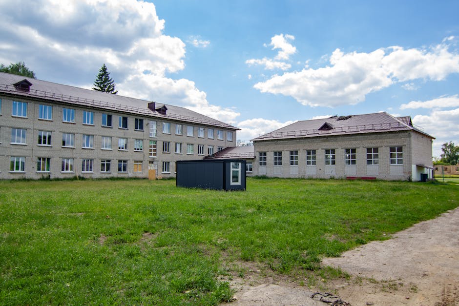 A three-story school structure surrounded by greenery and a clear sky.
