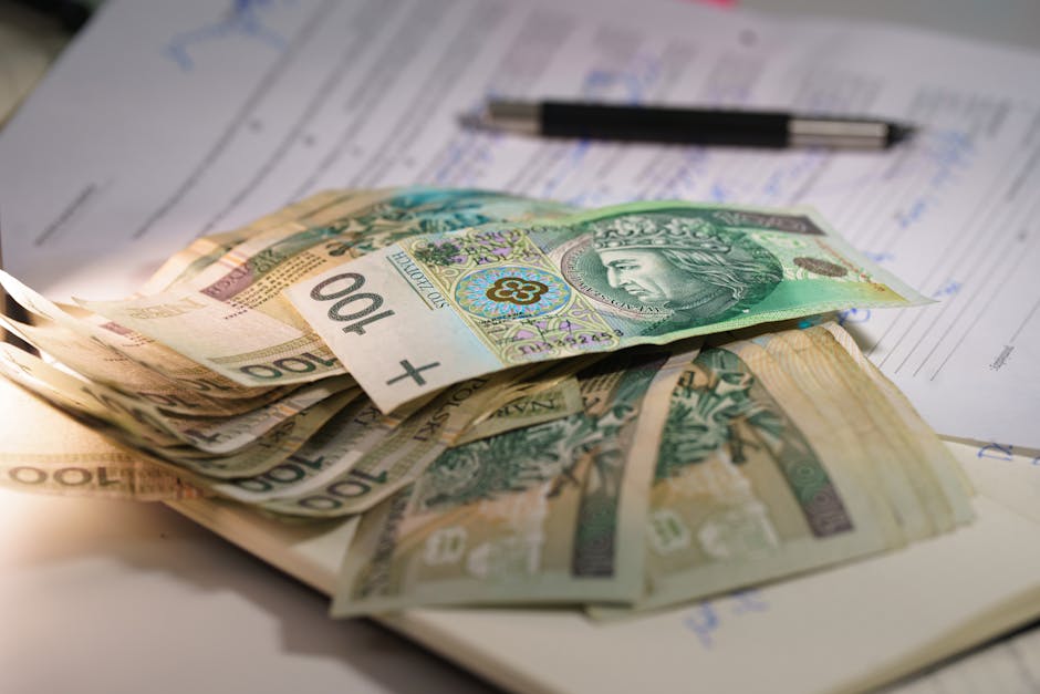 Stack of Polish zloty banknotes on financial documents with a pen, indicating monetary transactions in an office setting.