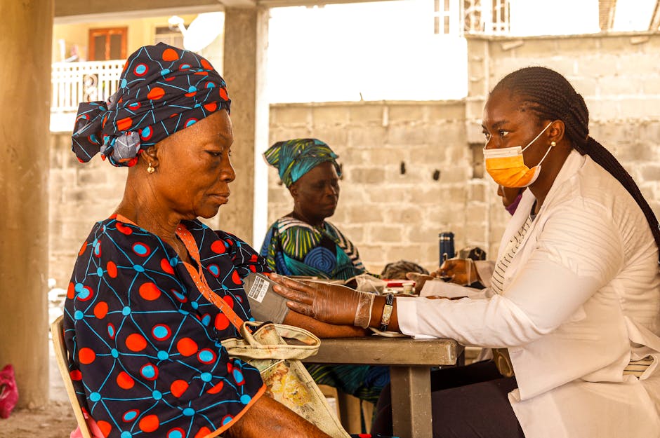 A healthcare worker checks blood pressure of an elderly woman in a rural clinic setting.