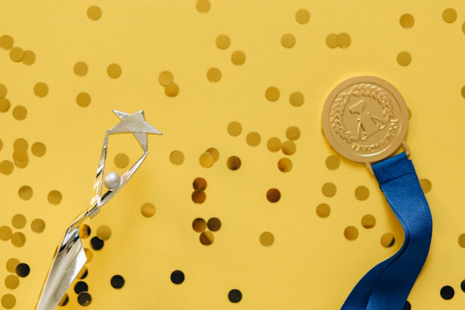 Golden medal and silver trophy with confetti on yellow surface, celebrating achievement.