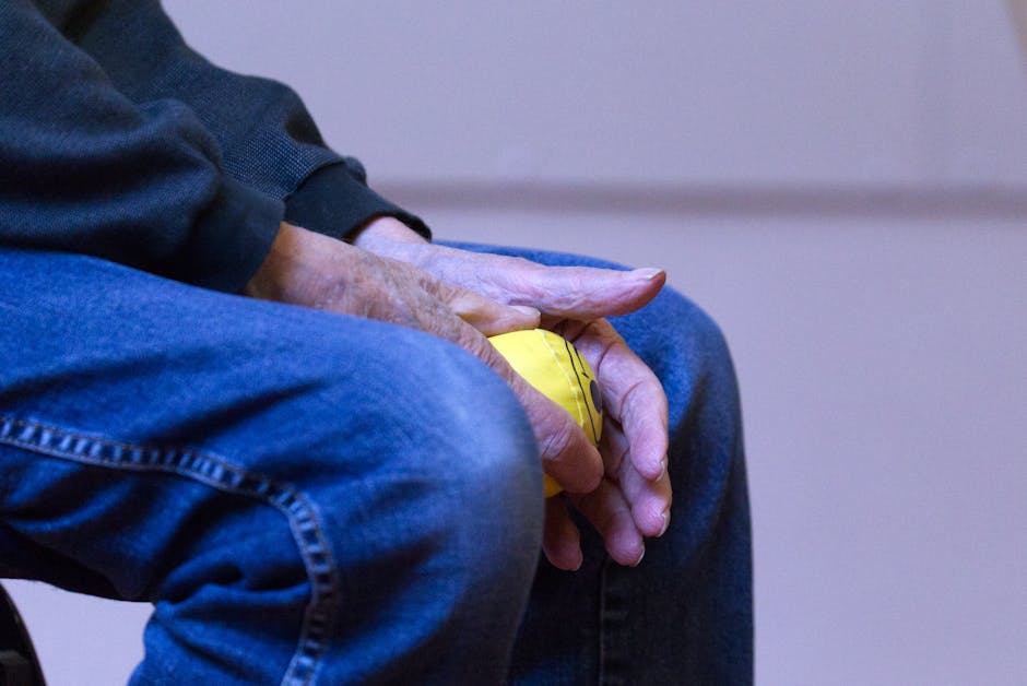 Elderly person holding a yellow stress ball in denim jeans, symbolizing relaxation and comfort.