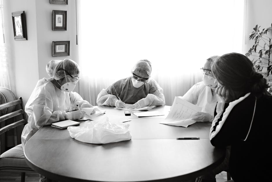 Group of healthcare workers in PPE having a discussion at a table indoors.
