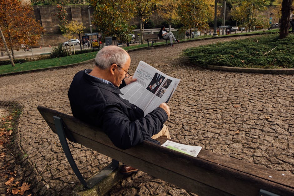 Senior man enjoys reading the newspaper while relaxing on a park bench in Porto, Portugal during autumn.