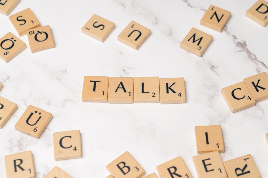 Wooden Scrabble tiles on a marble background spelling 'Talk', symbolizing communication and language.